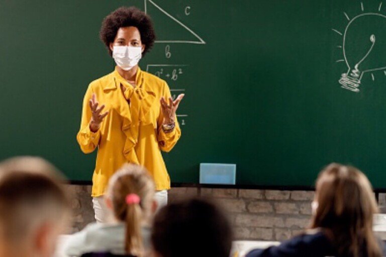 Black teacher with protective face mask teaching her students on a class at elementary school.